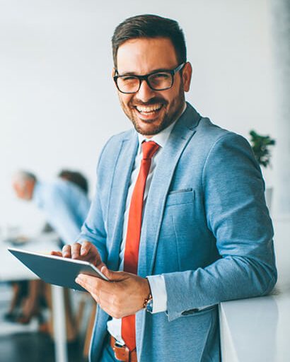 Confident businessman in a blue suit holding a tablet in a modern office, smiling while representing professional trade finance services.
